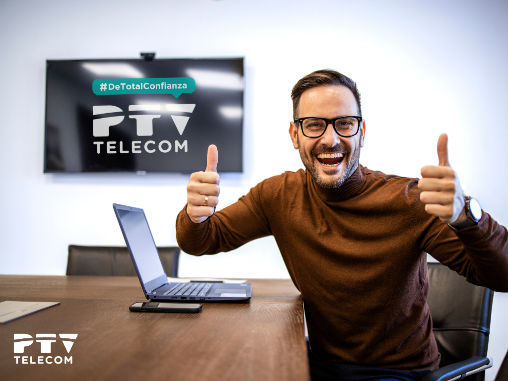 Hombre feliz con ordenador y televisión de fondo, celebrando la oferta de fibra óptica de 300Mb por solo 9,95€/mes con PTV Telecom.